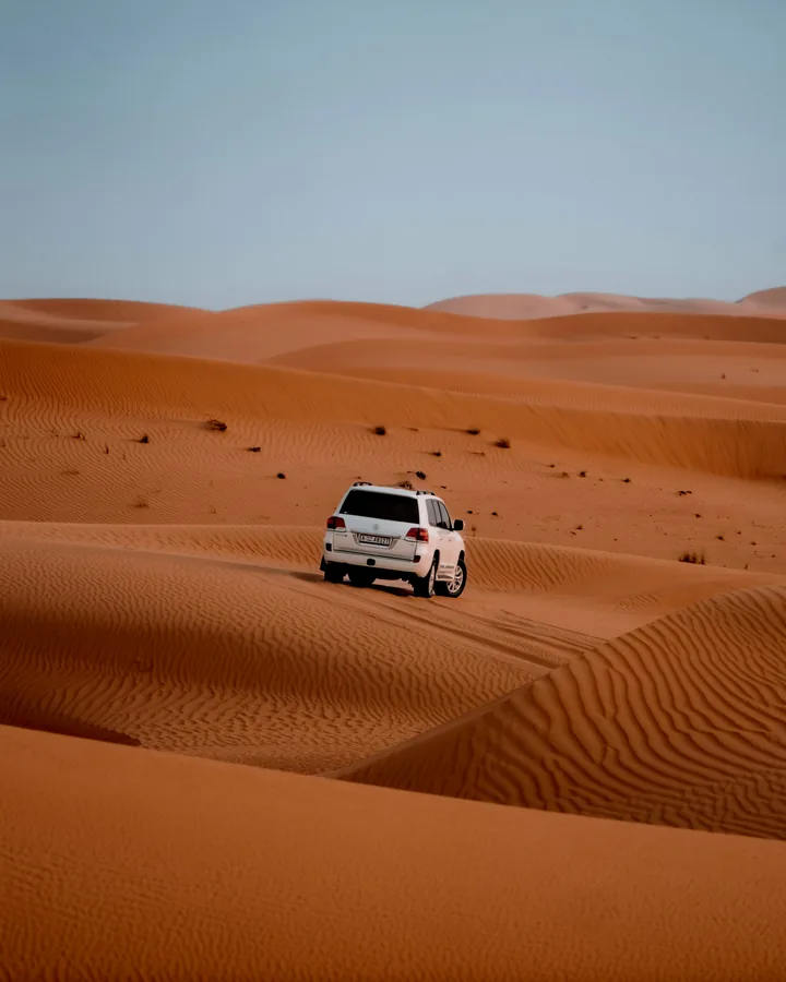 A safari vehicle travelling through rolling orange sand dunes in Dubai